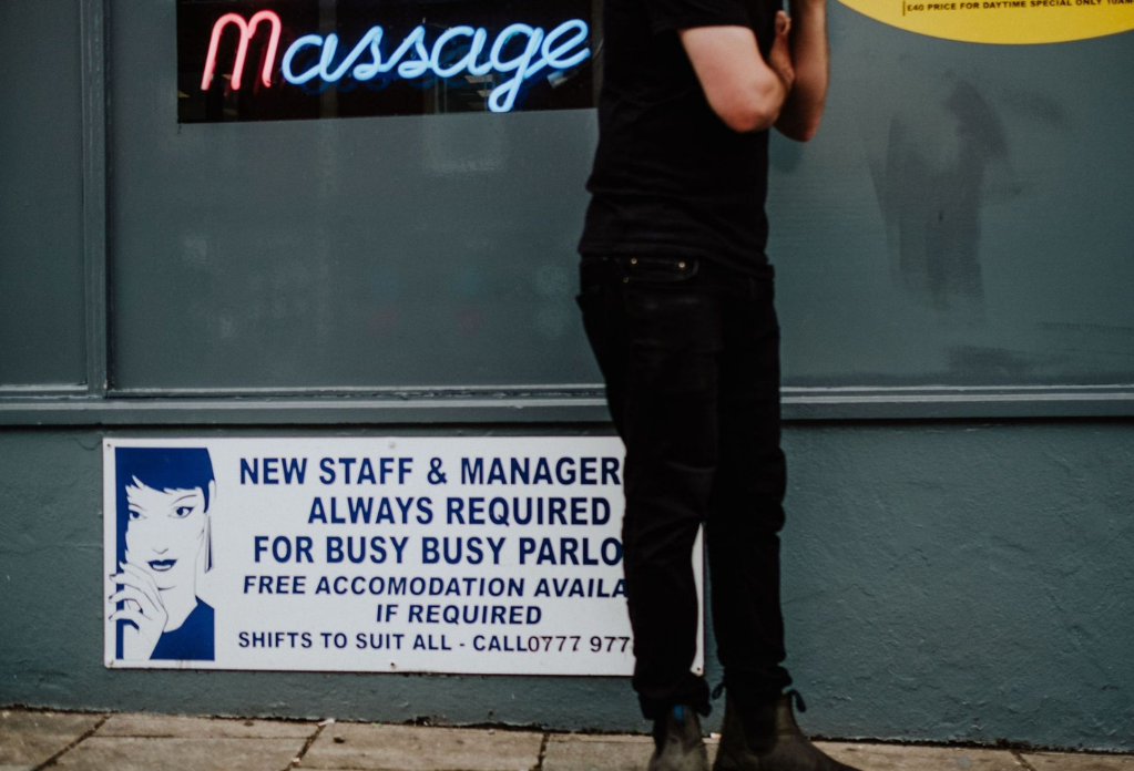 A man stands next to a sign for adult services making a phonecall