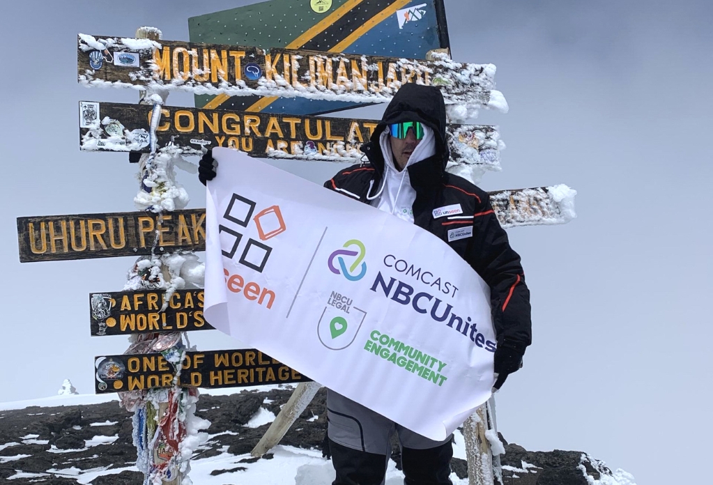Ian poses at the Uhuru Peak summit with an Unseen banner. Kilimanjaro climb to fight slavery.