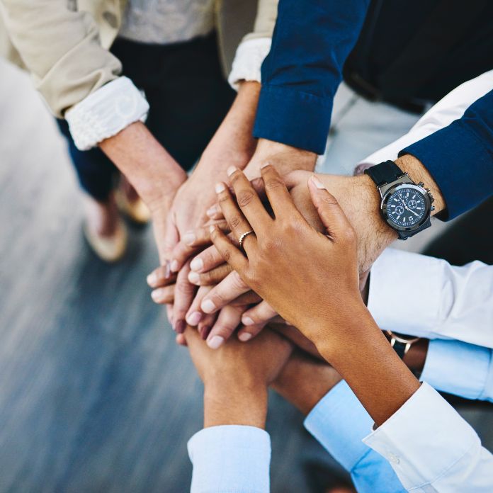 collaborative hubs A group of hands on top of one another to illustrate collaboration. The hands are diverse, with a mixture of skin tones.
